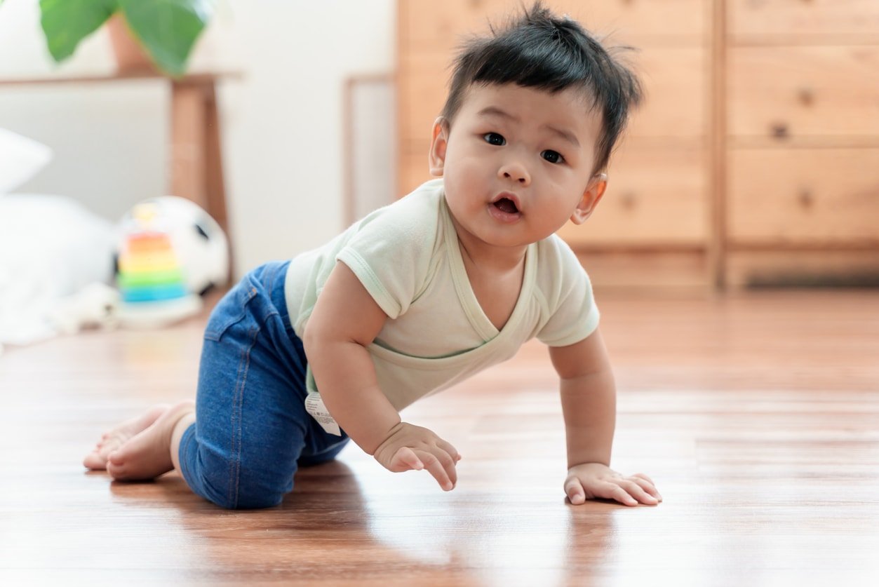 Retrato de um lindo menino asiático rastejando no chão em casa, sorrindo e olhando para a câmera.  Conceito de vida doméstica de bebê de família asiática.