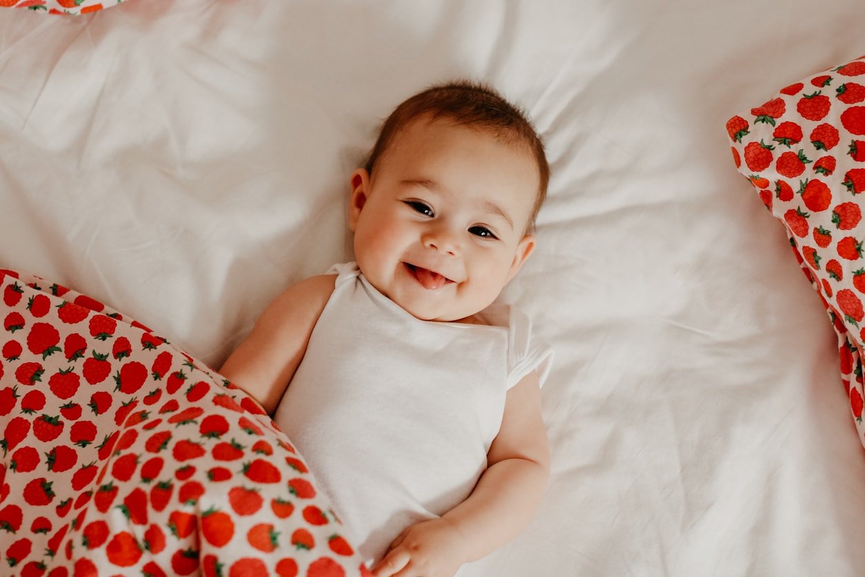Menina feliz deitada em uma cama com um cobertor de morango sorrindo para a câmera.