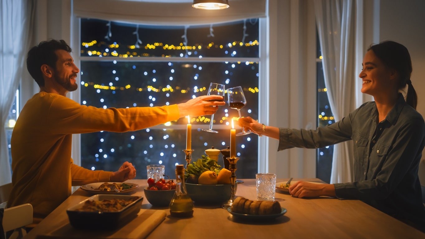 Feliz jovem casal apaixonado tem um jantar romântico, brindando com taças de vinho, comendo uma refeição saborosa na cozinha, comemorando, conversando.  Lindo adorável marido e mulher têm momentos românticos