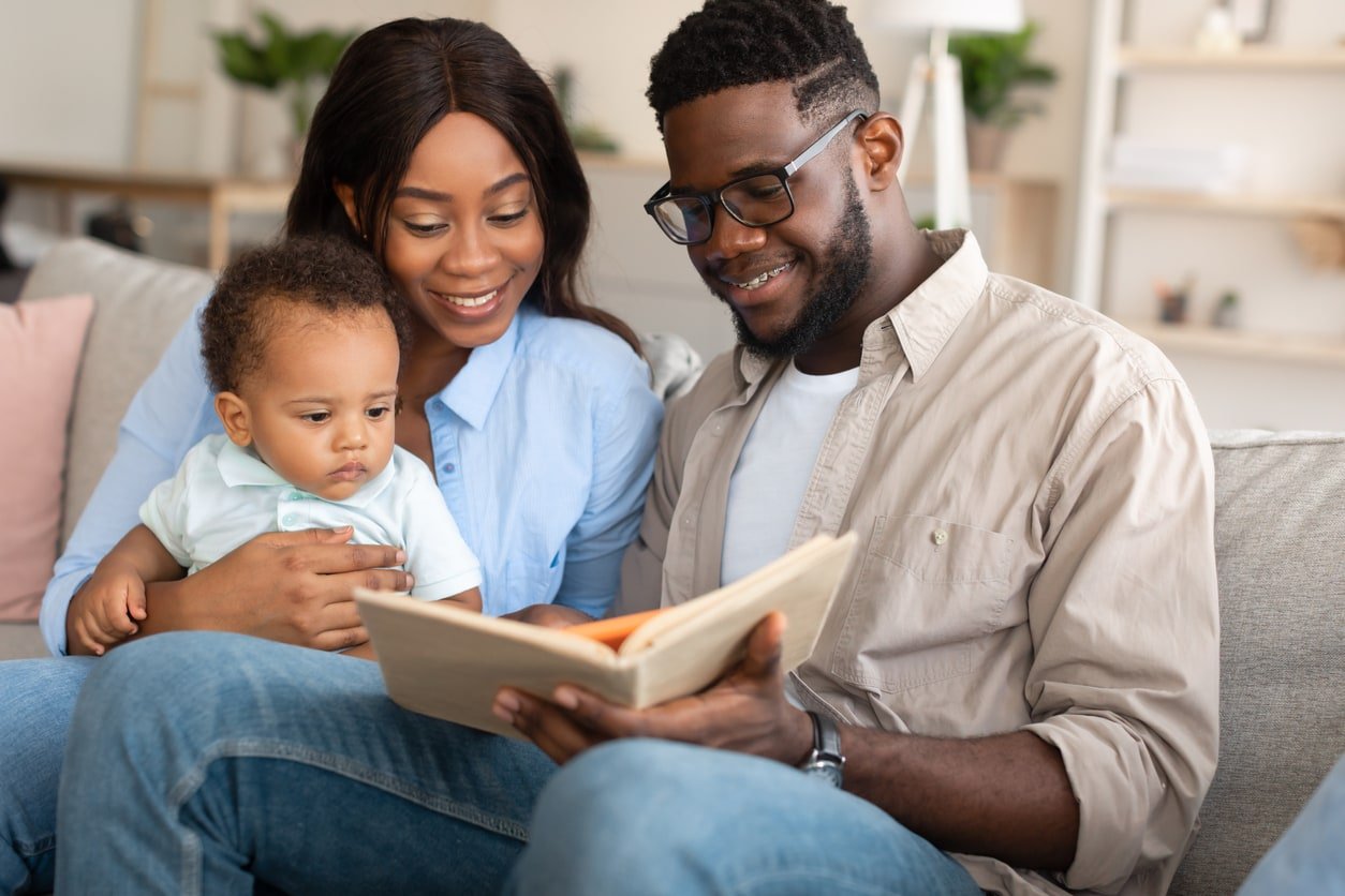 Retrato de pais negros da geração Y lendo um livro para seu adorável filho em casa, sentados no sofá de uma aconchegante sala de estar, passando tempo juntos.