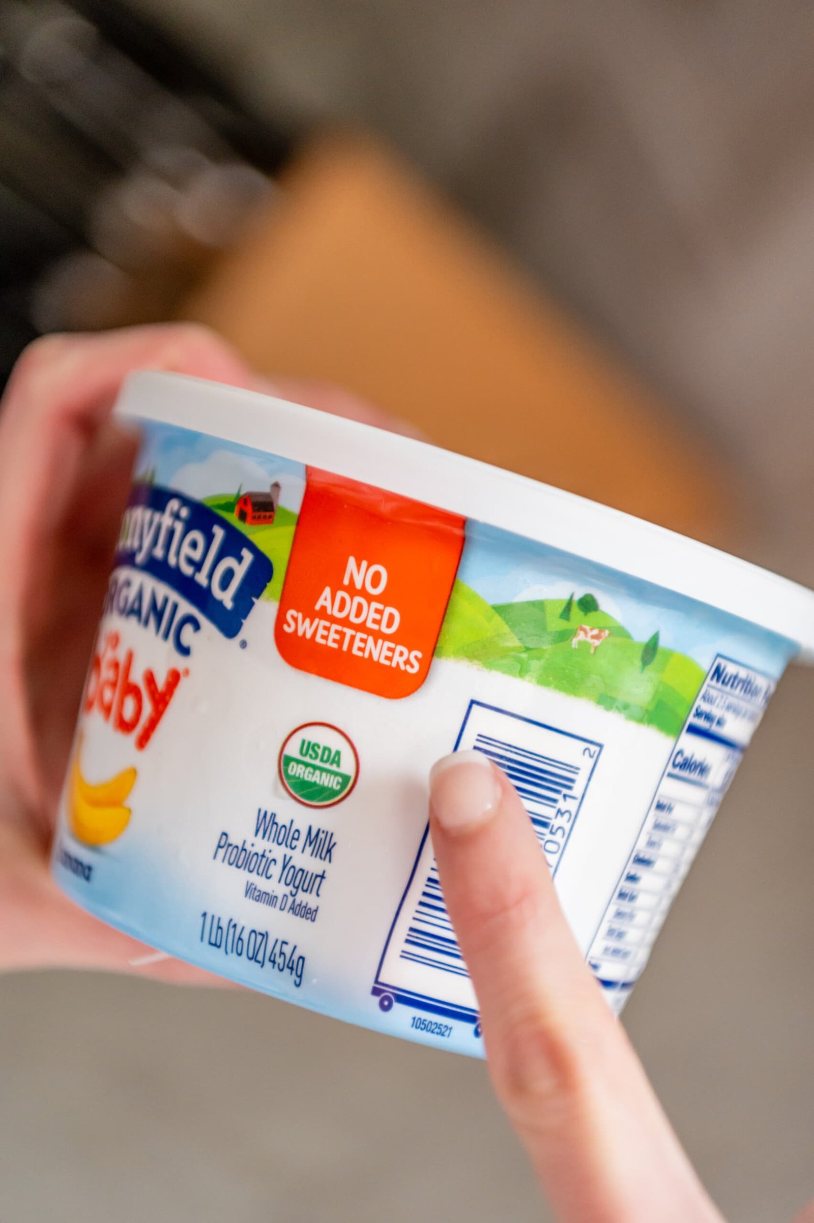 Um dedo bem cuidado apontando para a placa sem adição de adoçante na nova embalagem do iogurte Stonyfield Yobaby