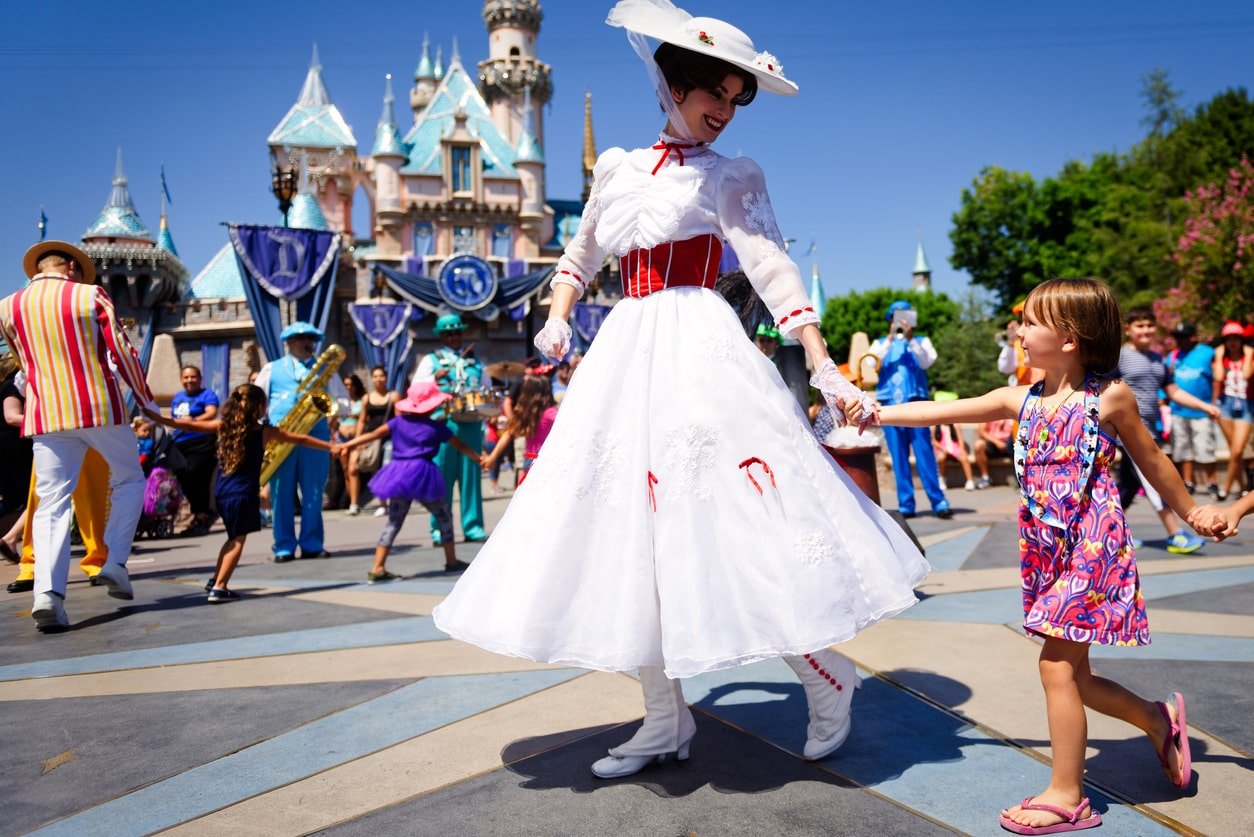 Mary Poppins sorri para uma criança enquanto lidera uma fila de crianças cantando e dançando em frente ao castelo da Cinderela durante a celebração do 60º Diamante da Disney.