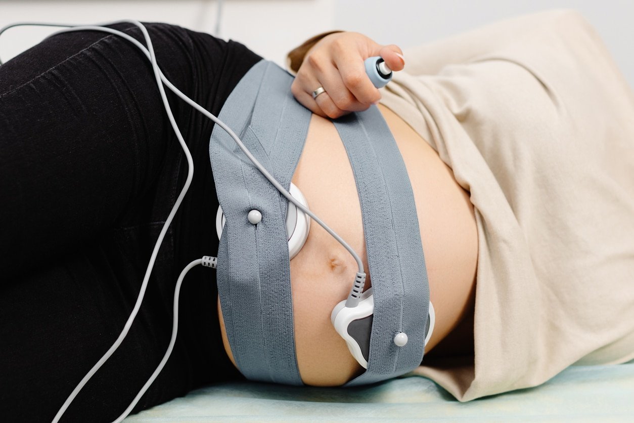 Mulher grávida verificando batimento cardíaco fetal por monitoramento fetal.  Gestante com parteira ajustando os sensores da cardiotocografia (CTG).