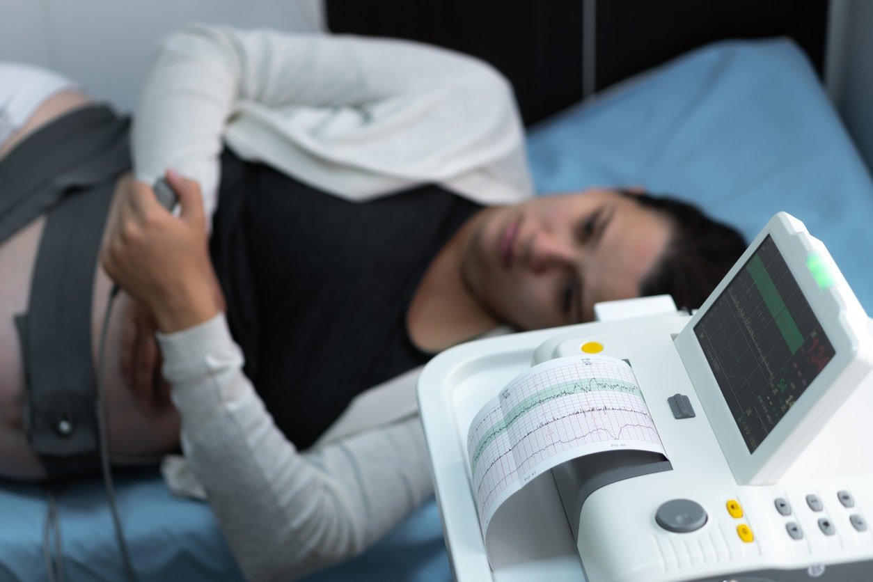 Mulher grávida no sofá do hospital durante cardiotocografia de controle médico.  Mãos do médico ginecologista ligam o consultor clínico do dispositivo CTG.  Examine o exame de saúde da mãe do bebê da barriga expectante.