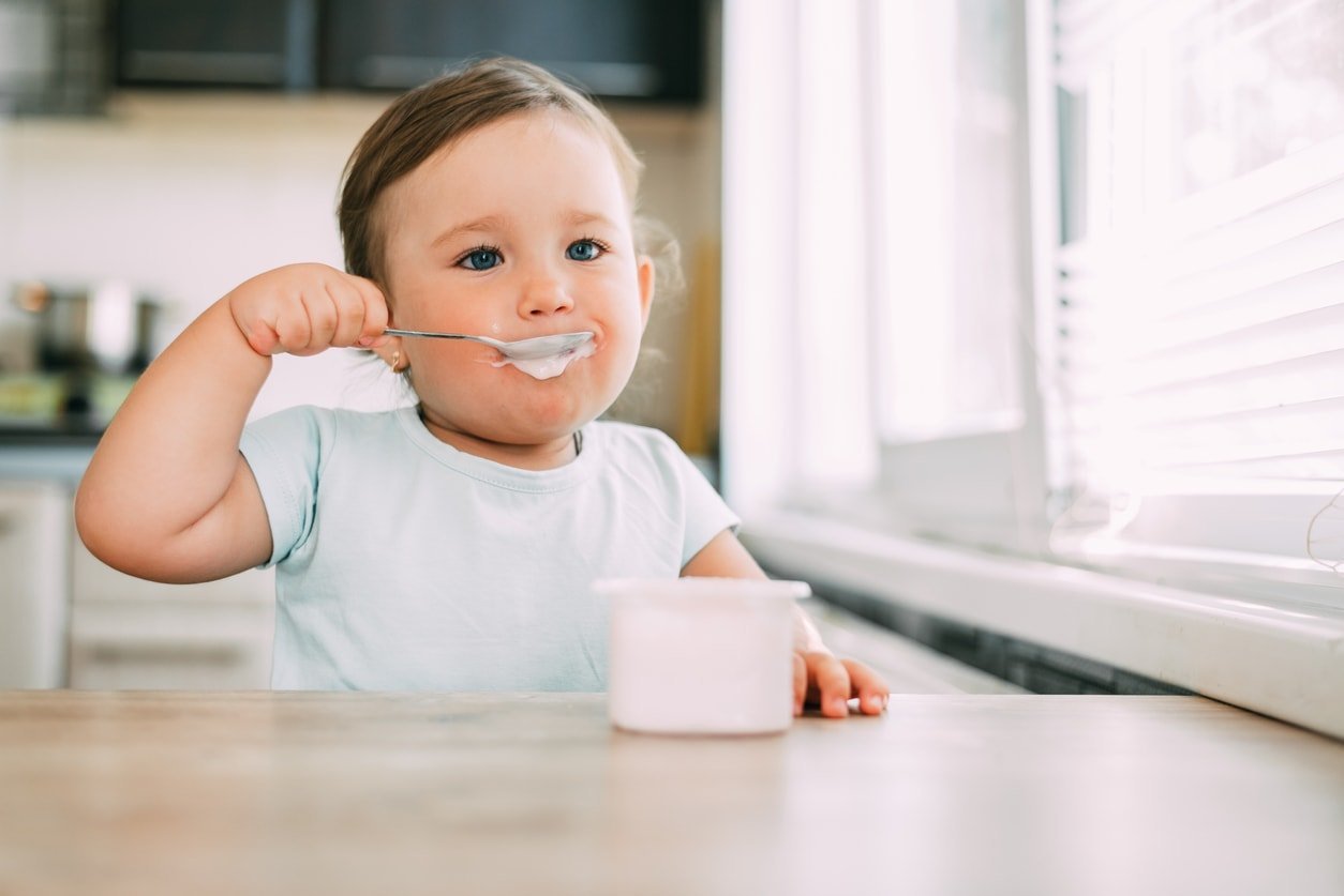 Menina à tarde na cozinha comendo iogurte é muito fofa