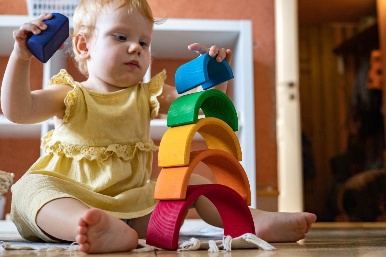 Menina com vestido elegante empilhando construção de bloco de arco arco-íris construindo torre de brinquedo de madeira ecológica.  Criança feliz brincando com materiais educacionais Montessori de desenvolvimento inicial em casa