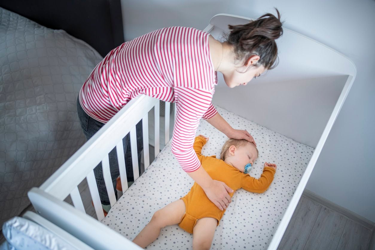 Jovem mãe carinhosa colocando seu filho para tirar uma soneca no berço.