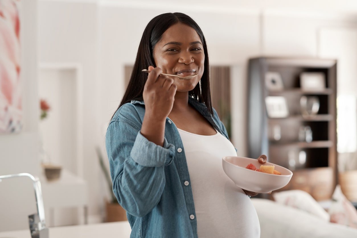 Retrato de uma mulher grávida comendo uma tigela de frutas em casa