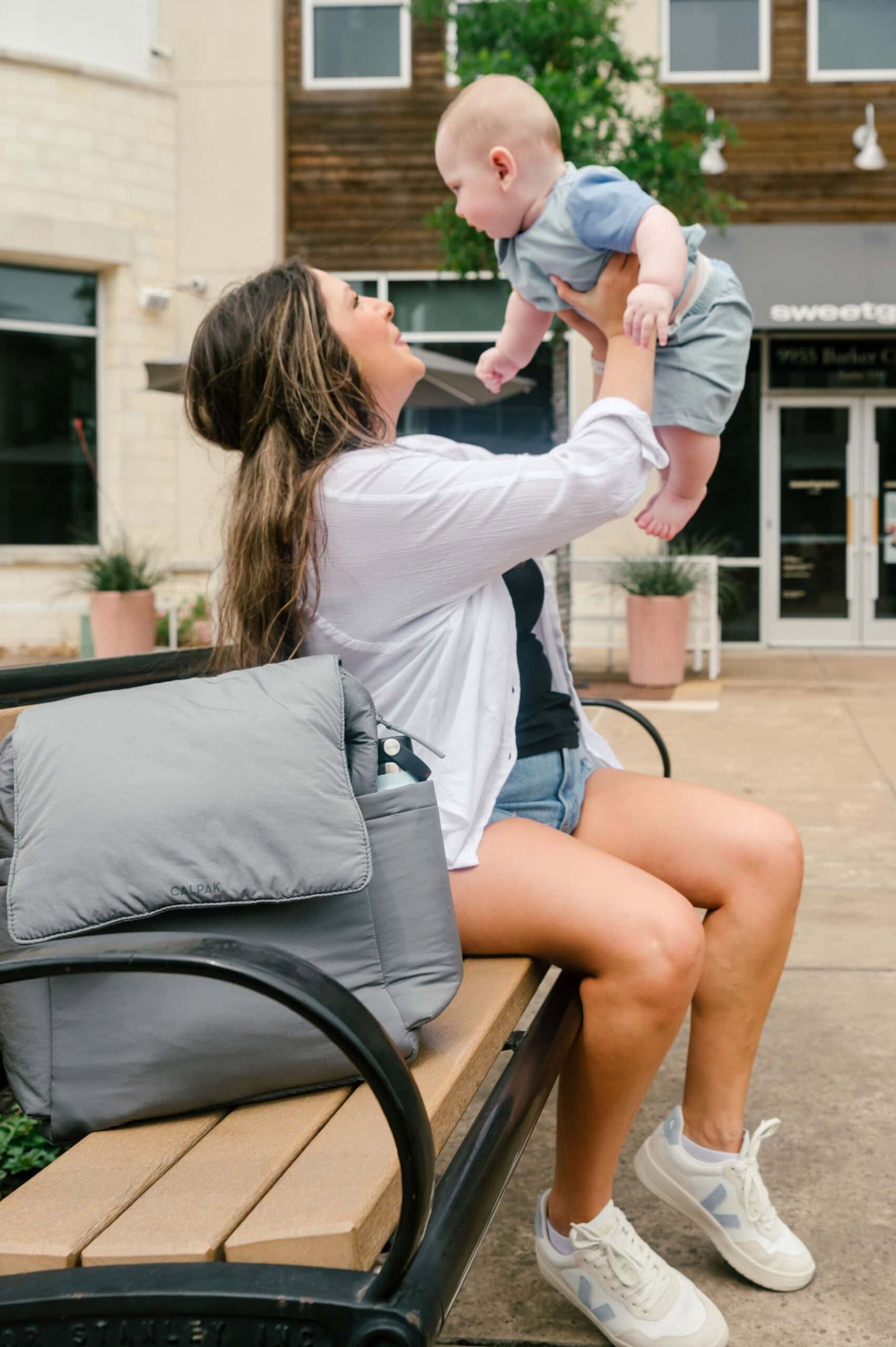 Mãe segurando o bebê com uma bolsa de fraldas CALPAK ao lado.