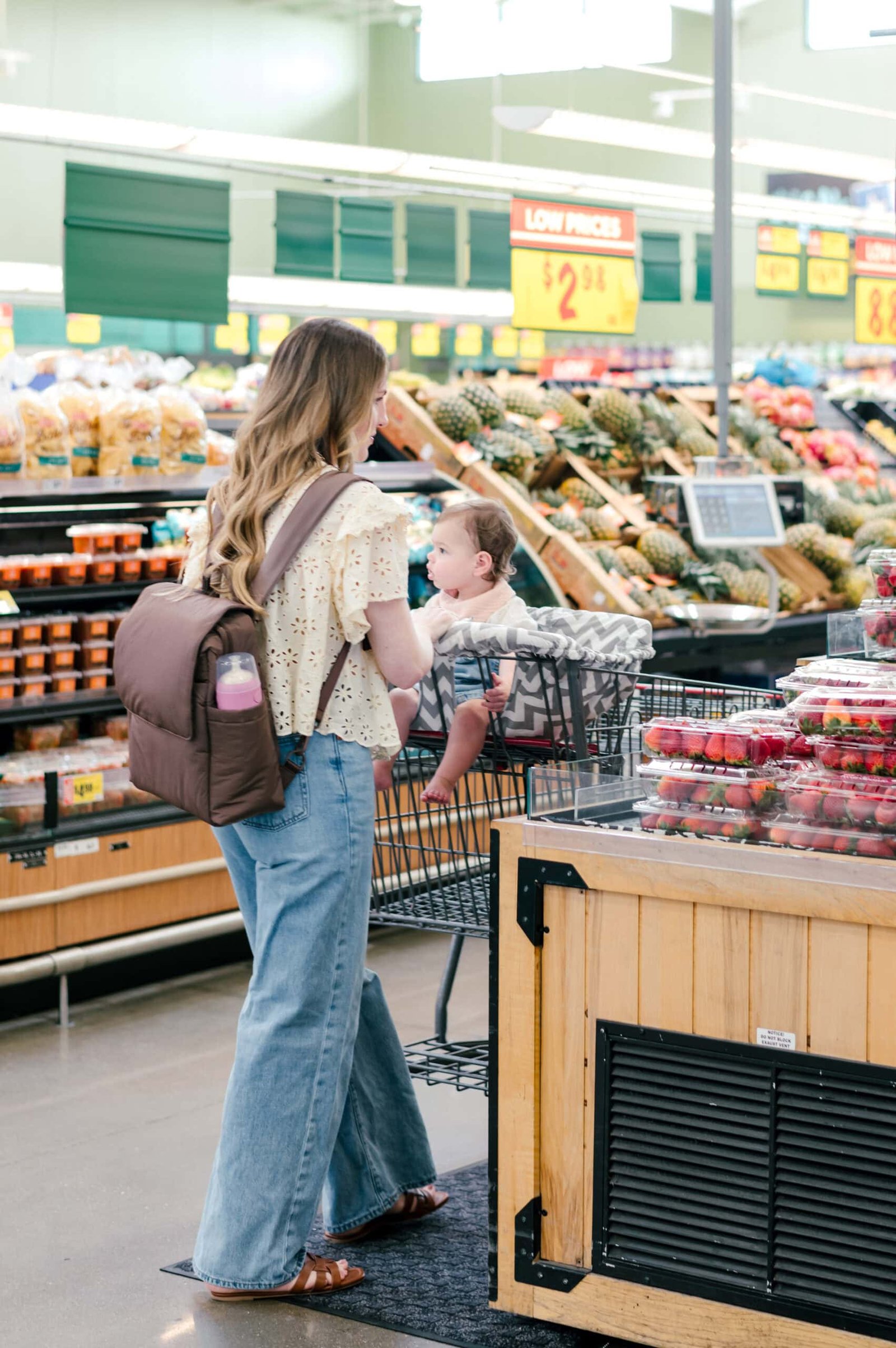 Mulher fazendo compras com seu bebê com sua mini mochila marrom CALPAK para fraldas
