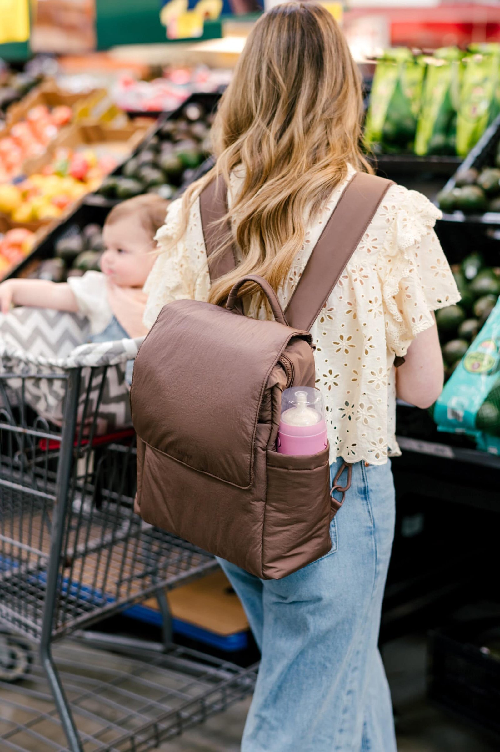 Mulher fazendo compras com seu bebê com sua mini mochila marrom CALPAK para fraldas