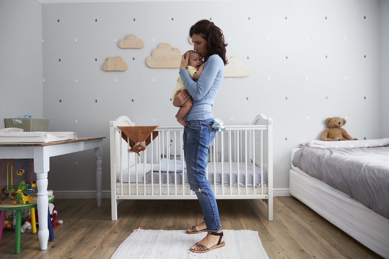 A woman stands in a nursery holding a baby, gently rocking to alleviate the baby