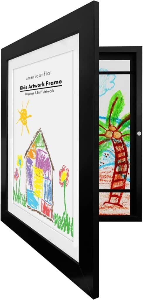 Uma moldura preta com um tapete branco exibindo um desenho colorido de uma criança de uma casa, sol e flores. A moldura aberta revela outro desenho de uma palmeira e praia dentro. O texto na moldura diz americanflat Kids Artwork Frame Displays 8.5x11 Artwork, perfeito para exibir obras de arte infantis.