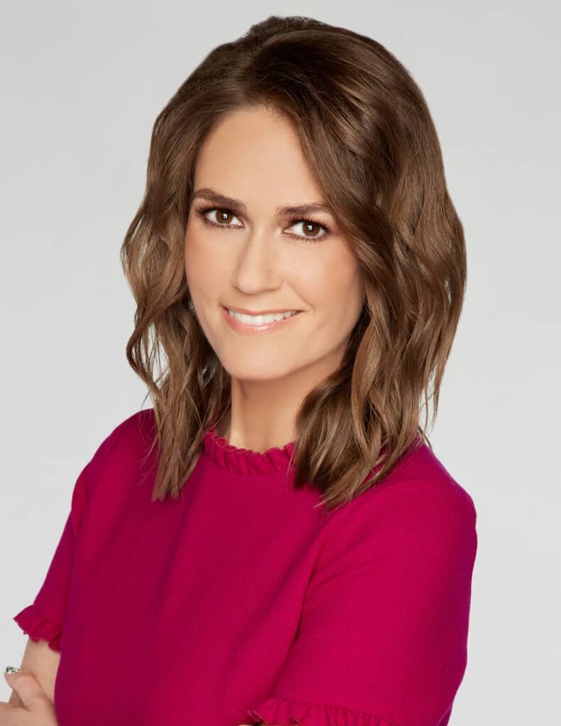 Jessica Tarlov com cabelos castanhos ondulados na altura dos ombros sorrindo enquanto olha para a câmera. Elas estão usando um top rosa brilhante com bordas franzidas. O fundo é branco liso.