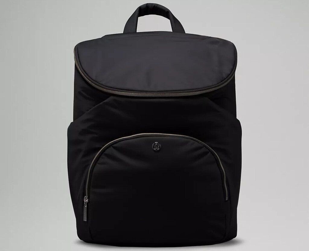 Uma mochila preta projetada pensando no futuro, perfeita para produtos para bebês para 2025, possui fecho de aba e um espaçoso bolso frontal com zíper. Centrada em um fundo liso, o design elegante da bolsa é completado com uma alça superior conveniente.