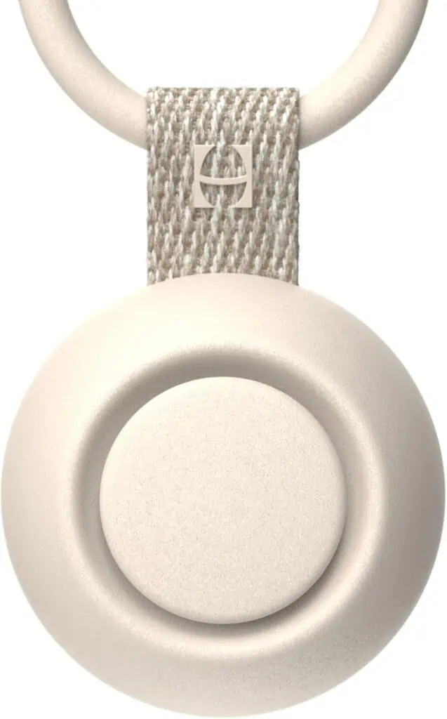 Close de um dispositivo circular branco preso a uma pulseira texturizada com um anel metálico, incorporando a estética moderna e elegante dos produtos para bebês para 2025. A pulseira apresenta um pequeno logotipo metálico quadrado, realçando seu design minimalista e cor clara.